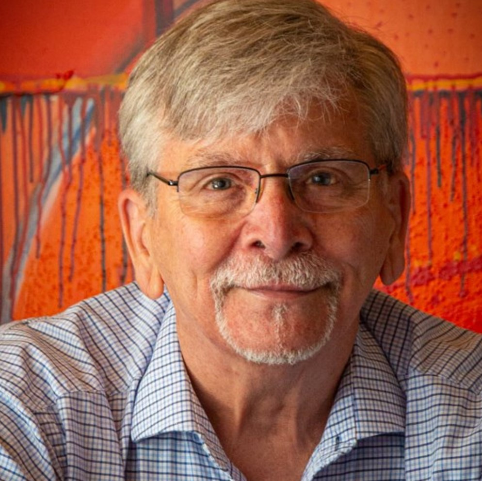 Portrait photograph of HB Barry Strasbourg-Thompson, smiling, in front of one of his paintings.
